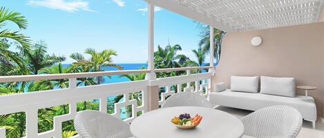 A balcony with a white railing, a white sofa, and a round table with a bowl of fruit.