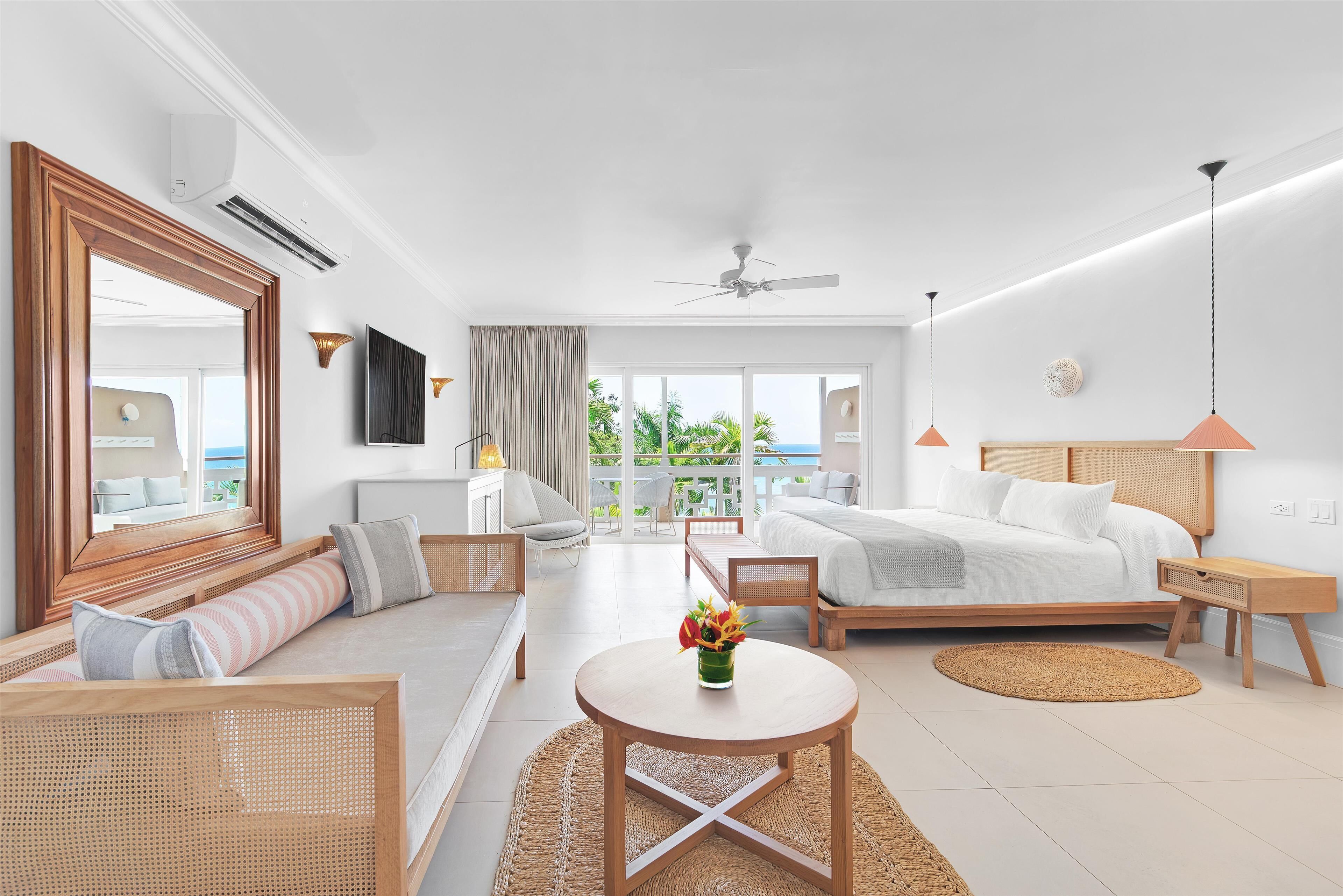A modern hotel room with a bed, sofa, and a balcony with a view.