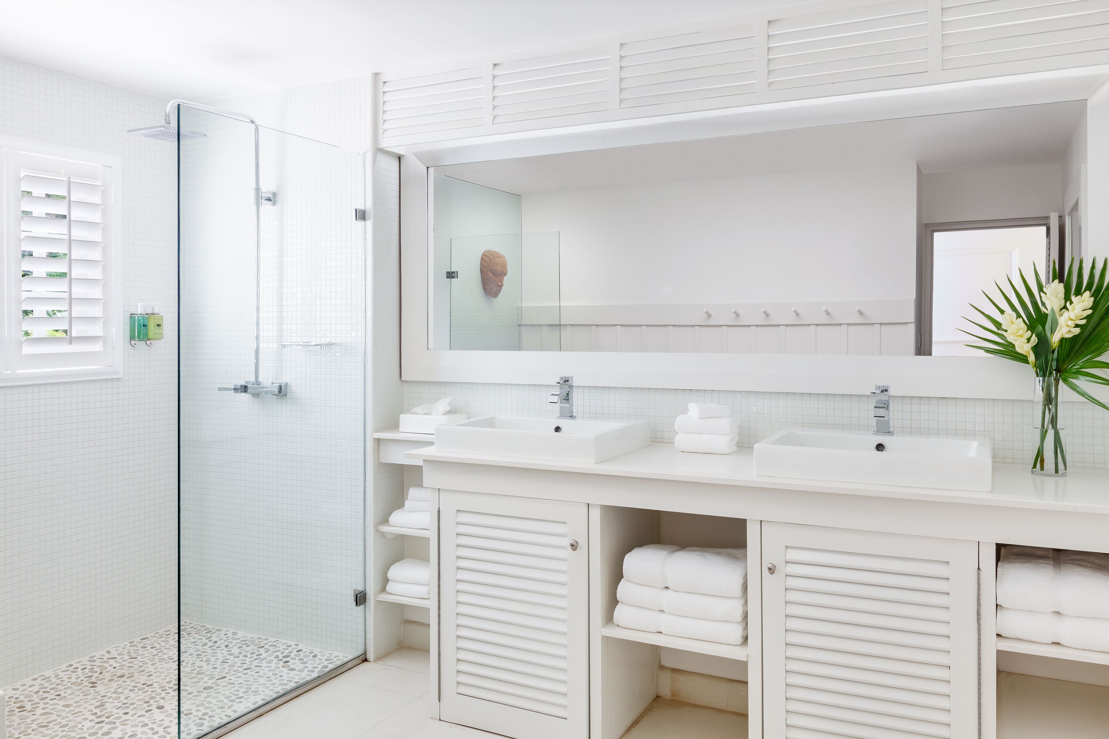 Une salle de bain moderne dotée d’une douche à parois de verre, de deux vasques, d’un grand miroir et de rangements intégrés pour les serviettes.