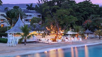 A beachfront resort with a pool, outdoor seating, and a gazebo.
