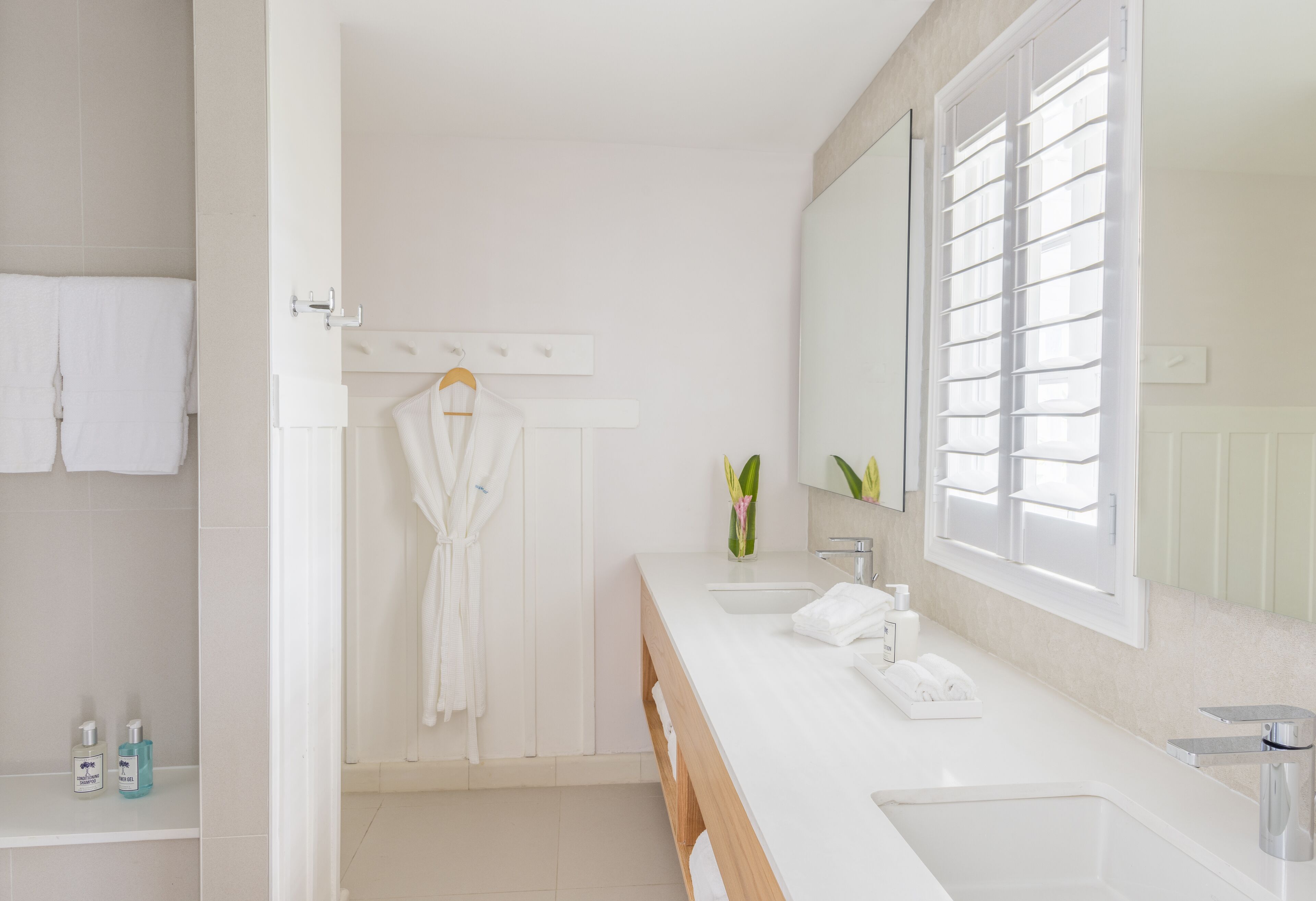 A modern bathroom with a large mirror, two sinks, a shower area, and a towel rack.