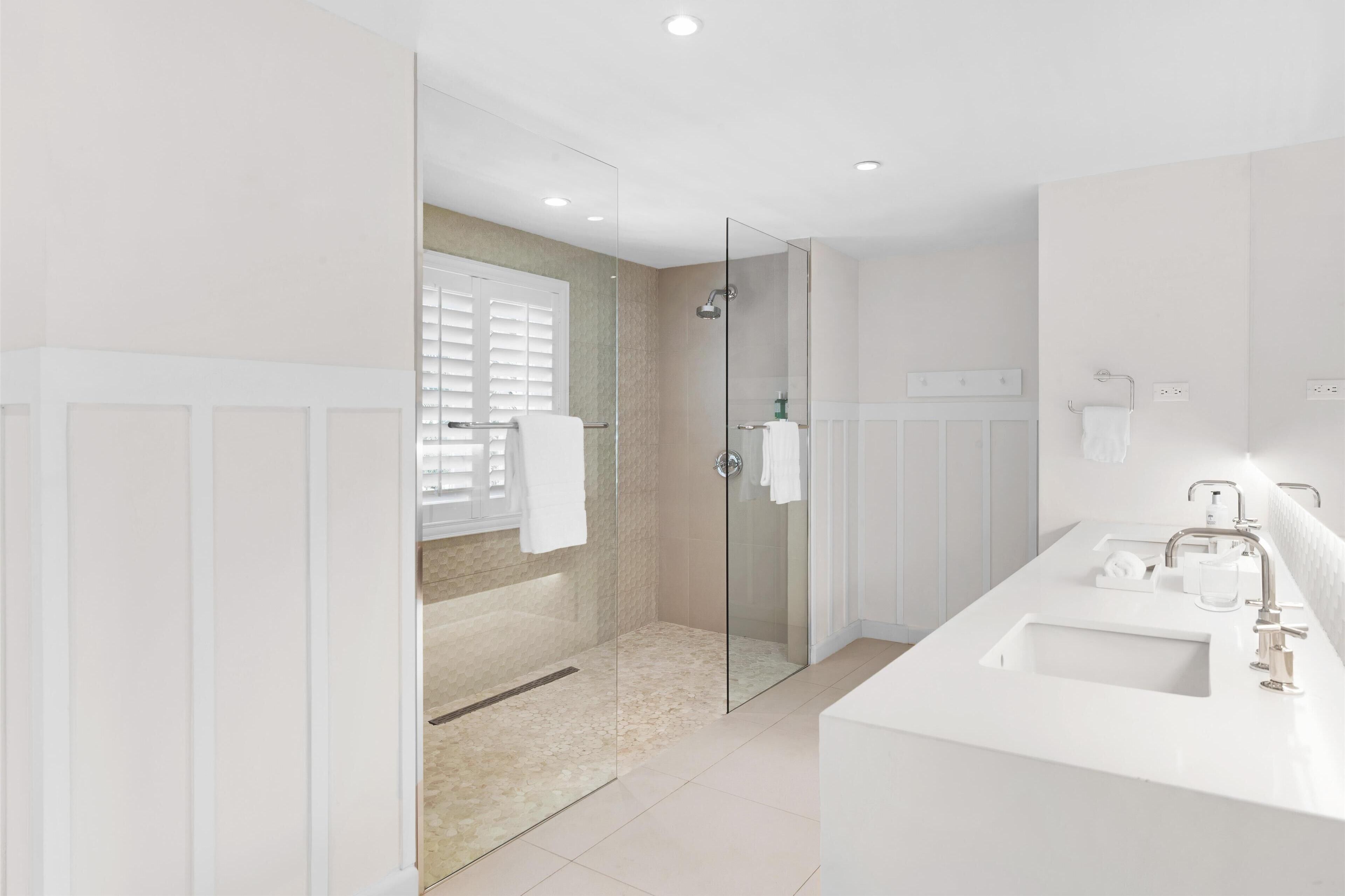 Un baño moderno con ducha de vidrio, lavamanos blanco y un espejo grande.