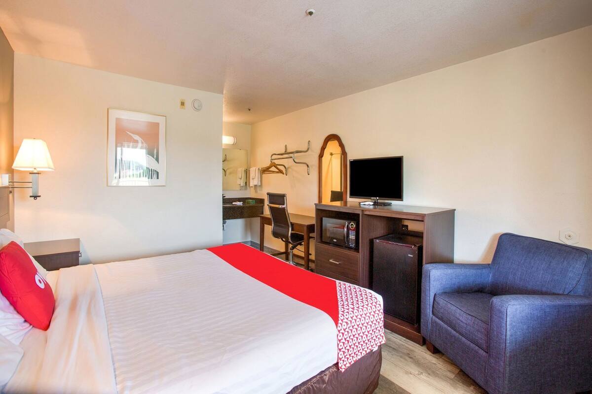 Una habitación de hotel con cama, escritorio, computadora, televisor, silla y espejo.