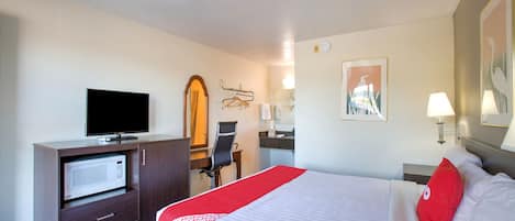 Habitación de hotel con cama, escritorio con televisor, espejo, silla y zona de baño.
