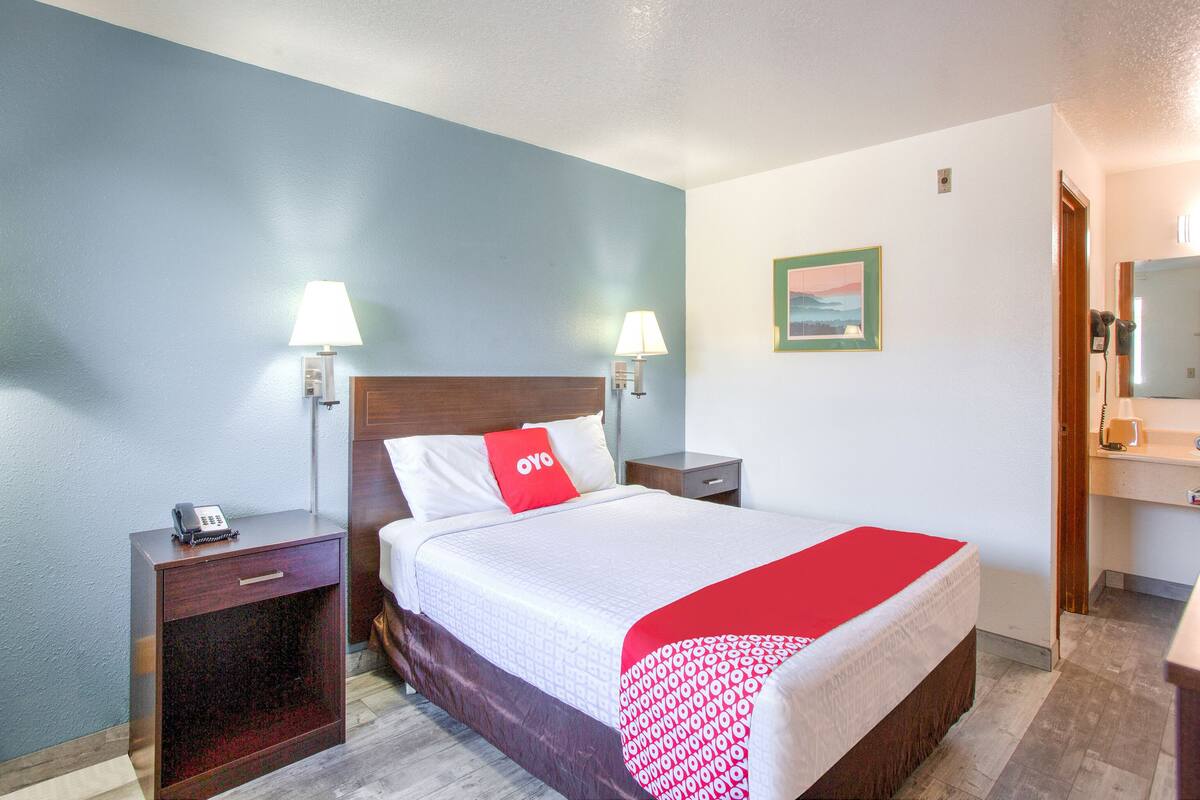 Habitación de hotel con cama, dos mesitas de noche, un escritorio, una silla, un espejo y una puerta.