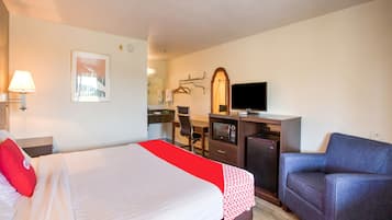 A hotel room with a bed, a desk with a computer, a TV, a chair, and a mirror.