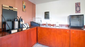 Una cocina compacta con estación de café, un lavamanos y un refrigerador antiguo.