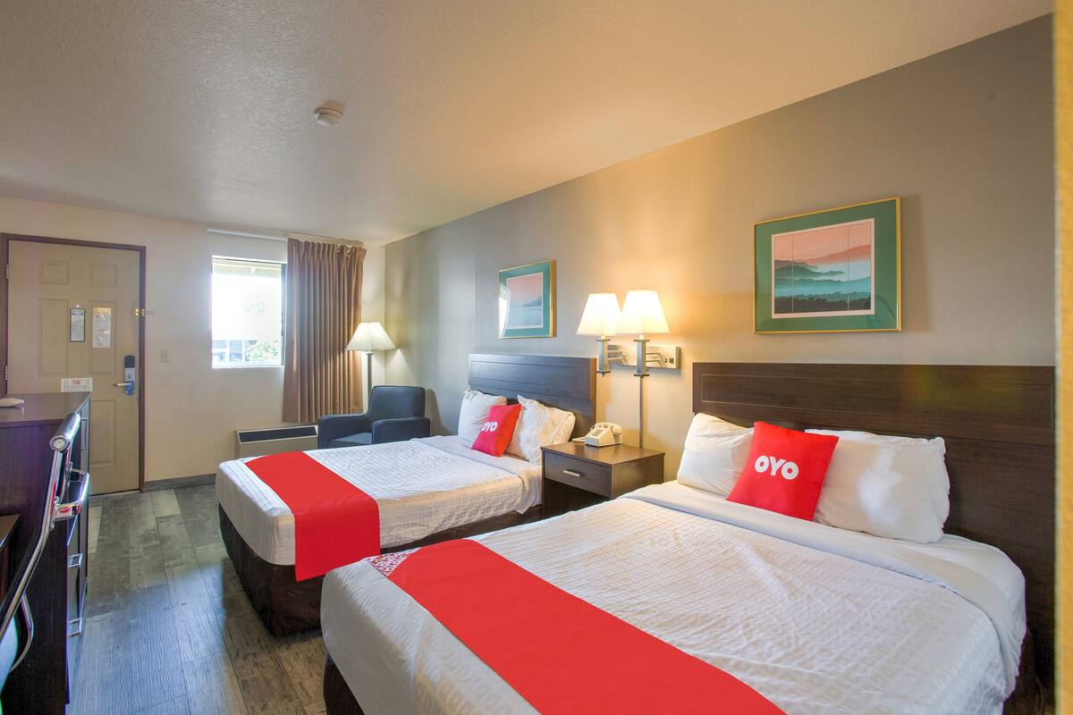 Una habitación de hotel con dos camas, un escritorio, una silla y un ventanal con cortinas.