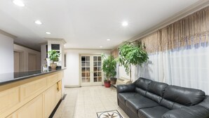 A modern hotel lobby with a black leather sofa, a reception desk, and potted plants. - Travelodge Salinas (Salinas)