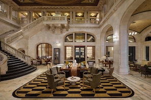 A grand lobby with a checkered floor, a staircase, and a seating area with chairs and tables.