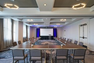 A conference room with a long table, chairs, a projector screen, and a whiteboard.