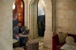 A hotel lobby with marble columns, a red sofa, and a person using a laptop at a small round table. - The Atterbury Hotel, Autograph Collection (Pittsburgh)