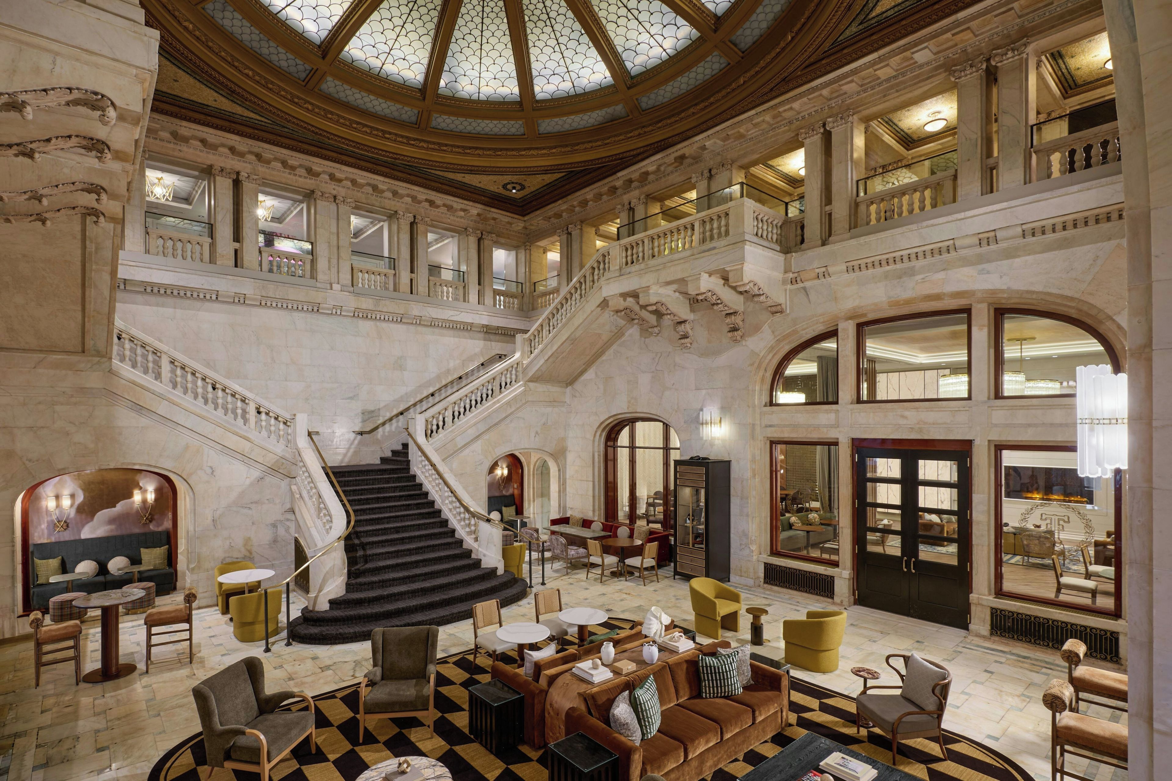 A grand lobby with a central staircase, multiple seating areas, and a high ceiling with a skylight.