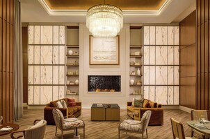 A spacious living room with a fireplace, marble-paneled walls, and a chandelier.