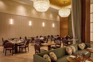 A hotel dining area with multiple tables and chairs, ambient lighting, and a patterned wall.