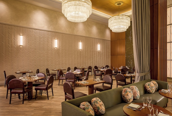 A hotel dining area with multiple tables and chairs, ambient lighting, and a patterned wall.