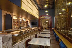 A bar area with marble-topped tables and chairs, a bar counter with a selection of bottles, and a staircase leading to an upper level.