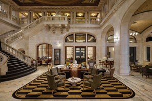 A grand lobby with a checkered floor, a staircase, and a seating area with armchairs and a coffee table.