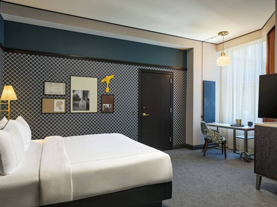 Quarto de hotel com cama, escrivaninha, televisão e guarda-roupa.