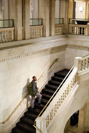 A person descending a marble staircase with balustrades, in a building with classical architecture.