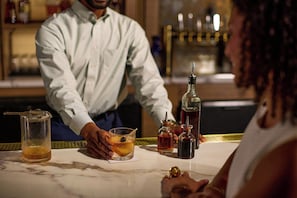 A bar setting with a bartender and a customer. There are various bottles and a glass on the counter.