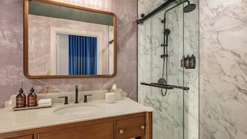 A bathroom with a marble shower, a sink with a mirror above it, and toiletries on the counter.