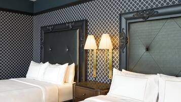 Quarto de hotel com duas camas, uma mesinha de cabeceira e uma luminária na parede.