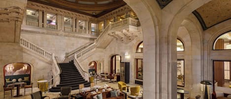 A grand lobby with a central staircase, multiple seating areas, and a high ceiling with skylights.