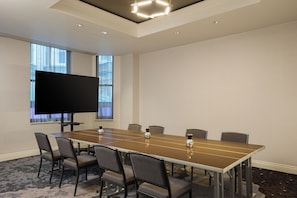 A conference room with a long table, six chairs, a flat-screen TV, and a window with blinds. - The Atterbury Hotel, Autograph Collection (Pittsburgh)
