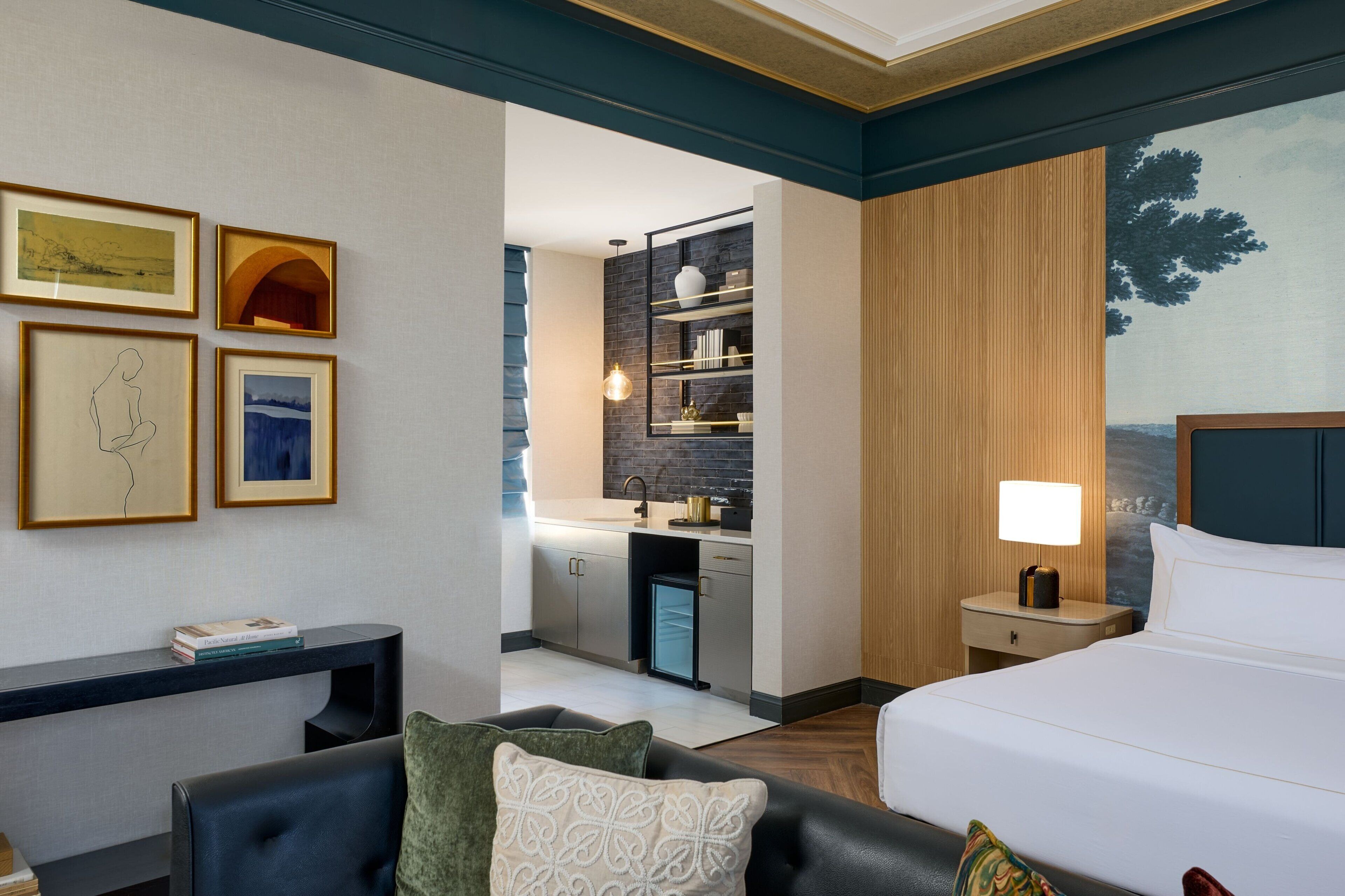 A hotel room with a bed, a desk, a chair, a nightstand, and a painting on the wall.