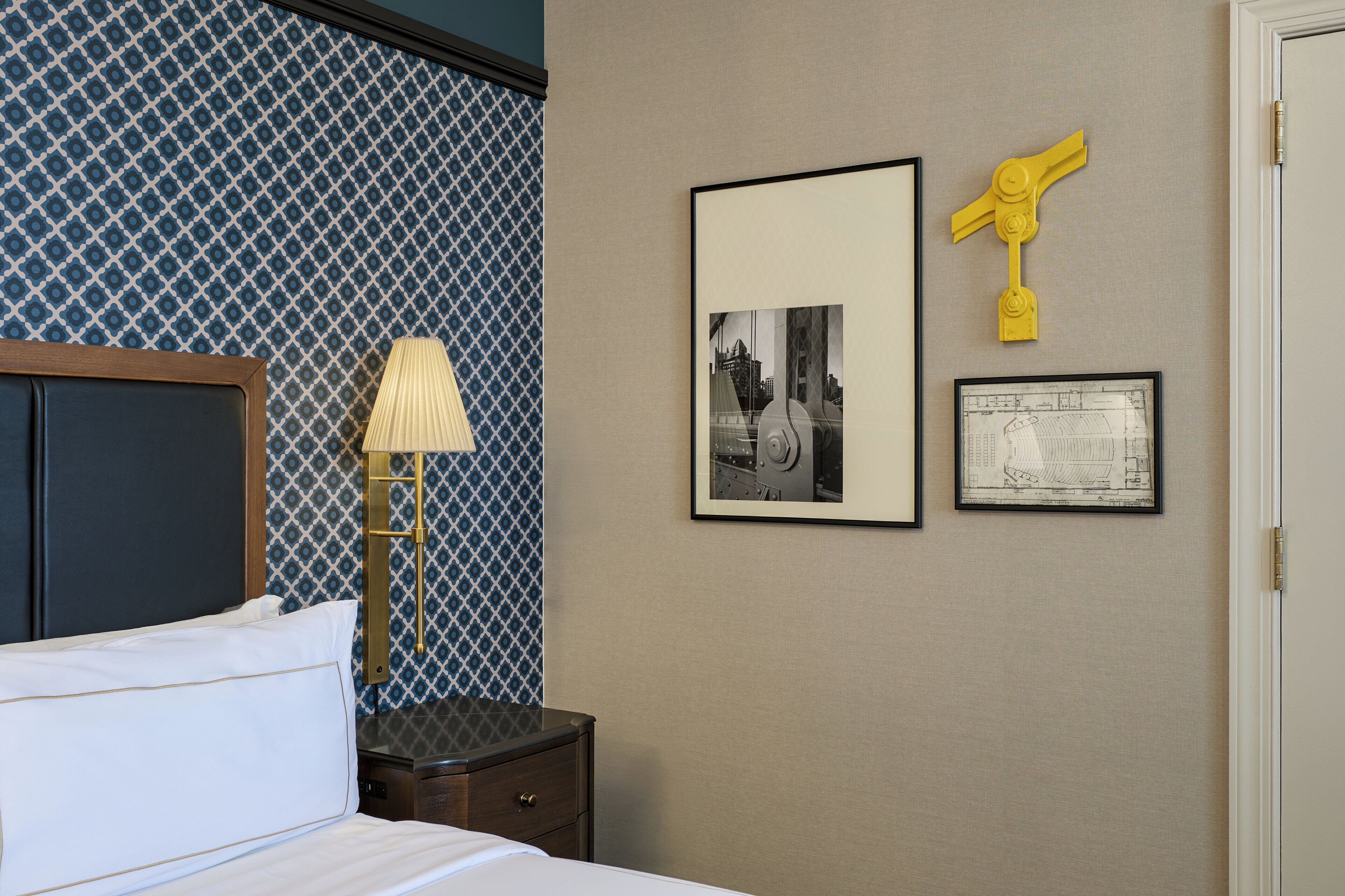 Habitación de hotel con cama, mesita de noche, lámpara y dos cuadros en la pared.