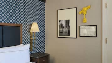 Habitación de hotel con cama, mesita de noche, lámpara y dos cuadros en la pared.
