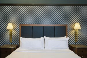 Una cama bien hecha con sábanas blancas y dos lámparas de noche sobre mesitas de madera.