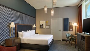 A hotel room with a large bed, bedside tables, a desk, a chair, and a television.
