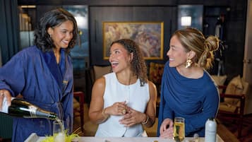 Three people at a table with a bottle of champagne, a glass, and various items on the table.