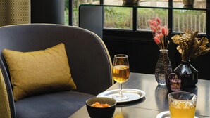 A dining area with a table set for two, featuring a bowl of fruit, two glasses of a beverage, and decorative vases.