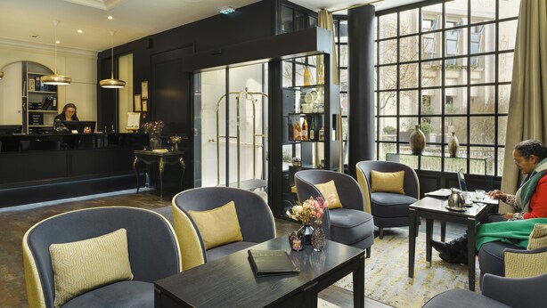 A modern hotel lobby with a reception desk, seating area, and large windows offering views of the city.