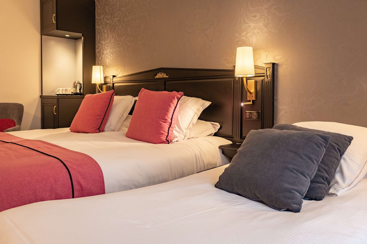 Une chambre d’hôtel avec deux lits, chacun doté d’une tête de lit, de tables de chevet, de lampes et d’oreillers.