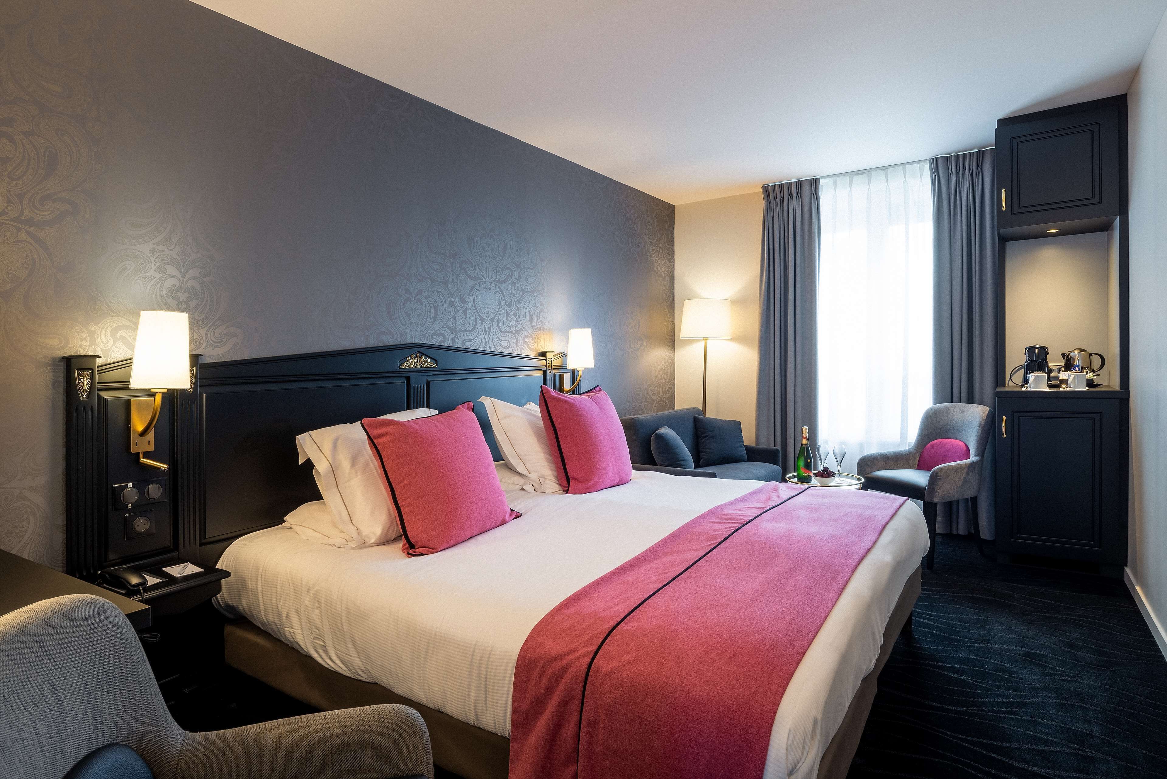A hotel room with a large bed, two bedside tables, a desk, a chair, a wardrobe, and a window with curtains.