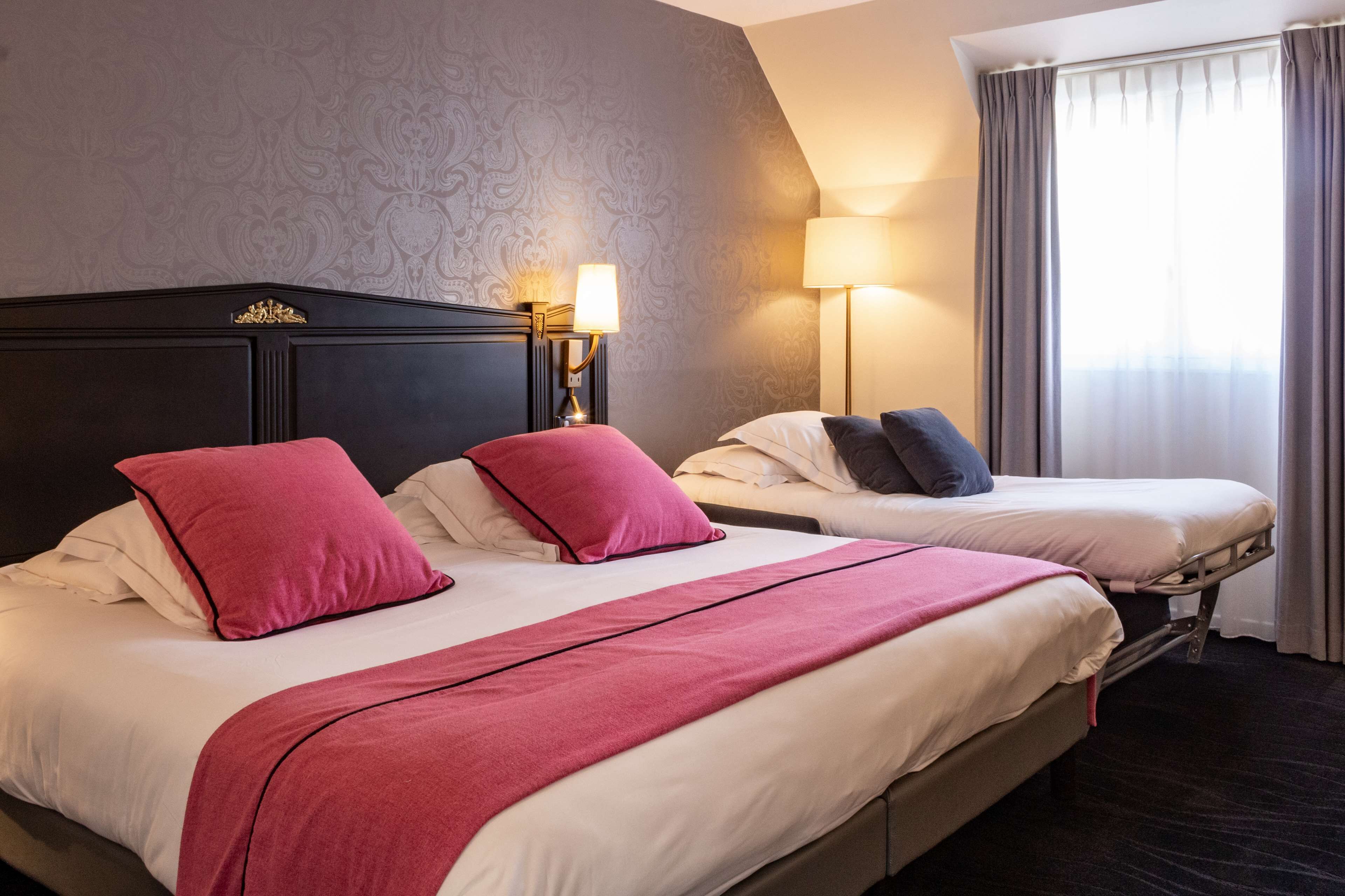 Una habitació d'hotel amb dos llits, cadascun amb capçalera, una taula de nit amb làmpada i una finestra amb cortines.
