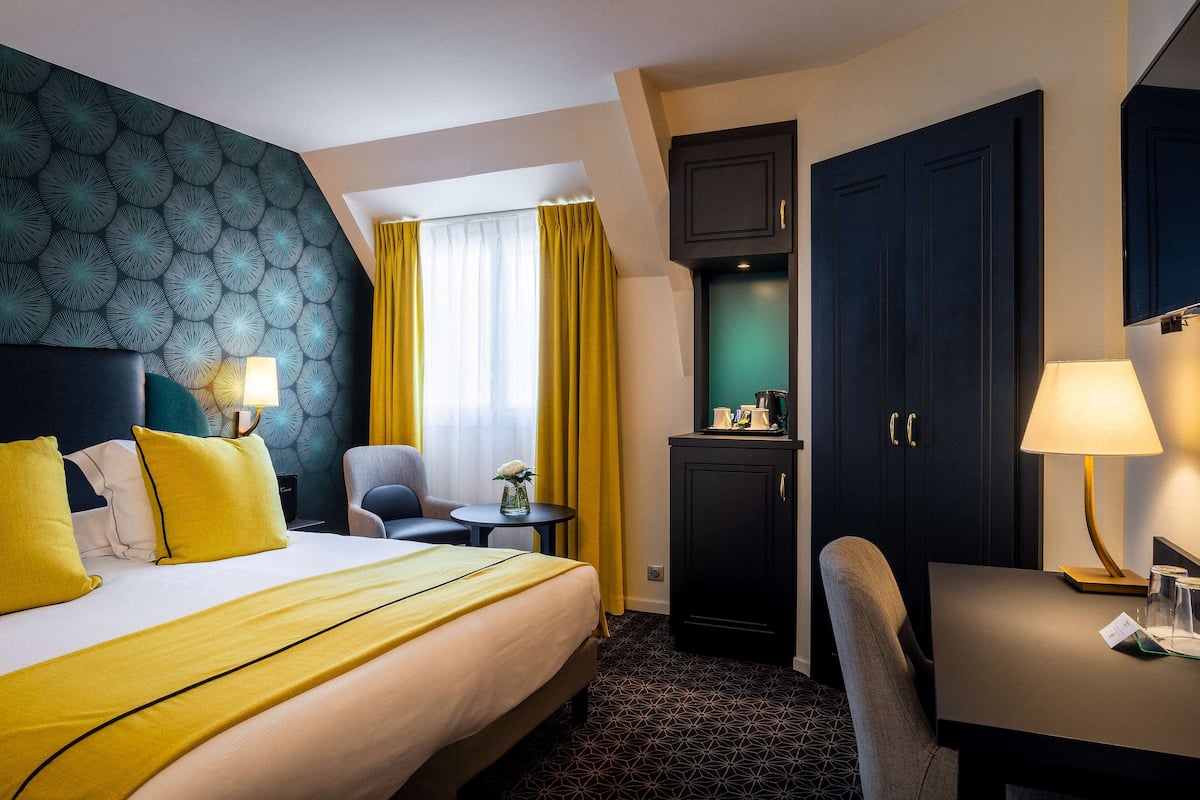Une chambre d’hôtel équipée d’un lit, d’un bureau, d’une chaise, d’une petite table, d’une lampe et d’une armoire.
