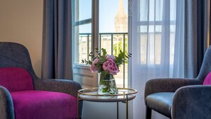 A room with two armchairs, a small table with a vase of flowers, and a view of a building through a window.