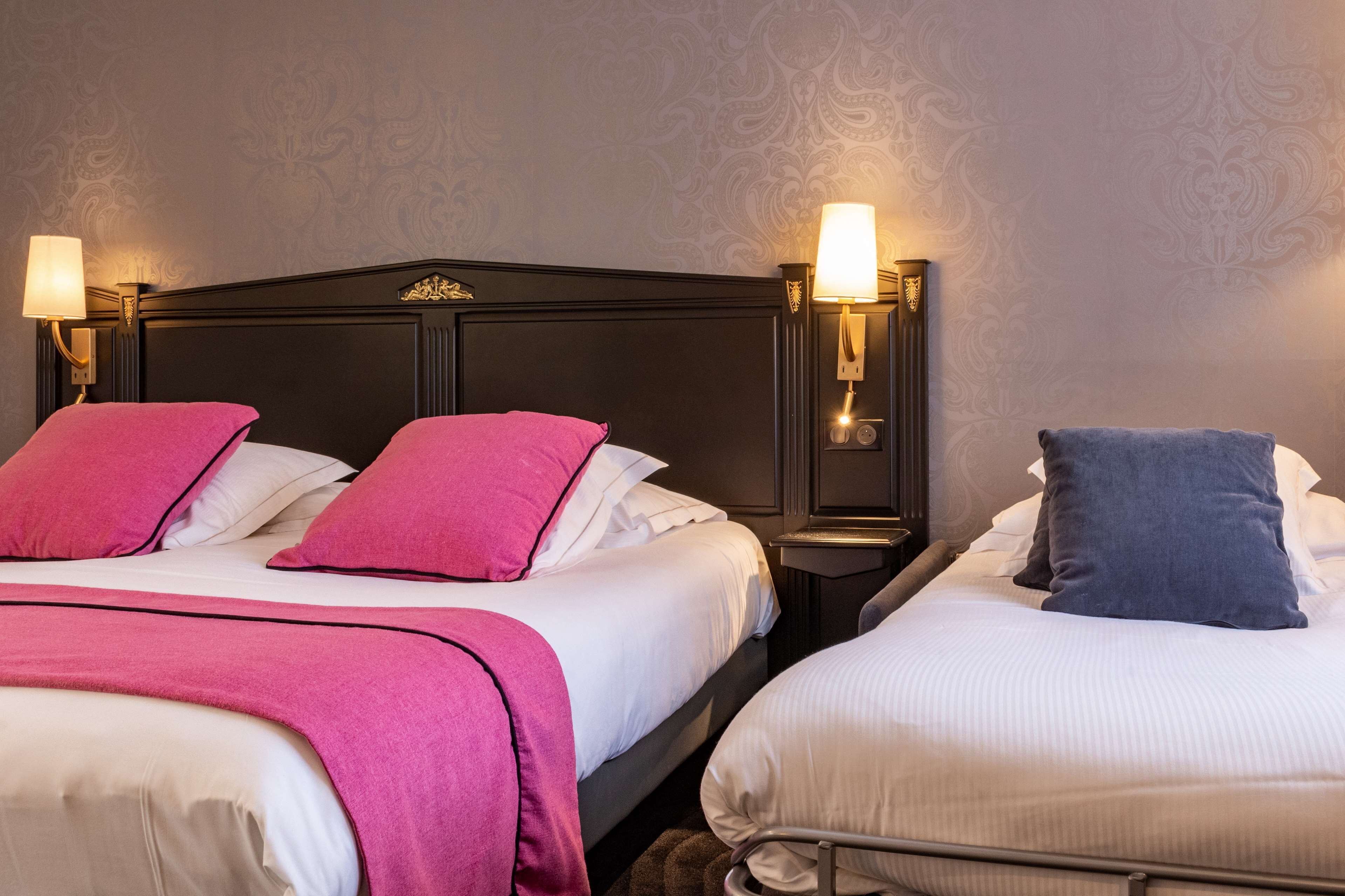 A hotel room with two beds, each with a headboard and bedside lamps.