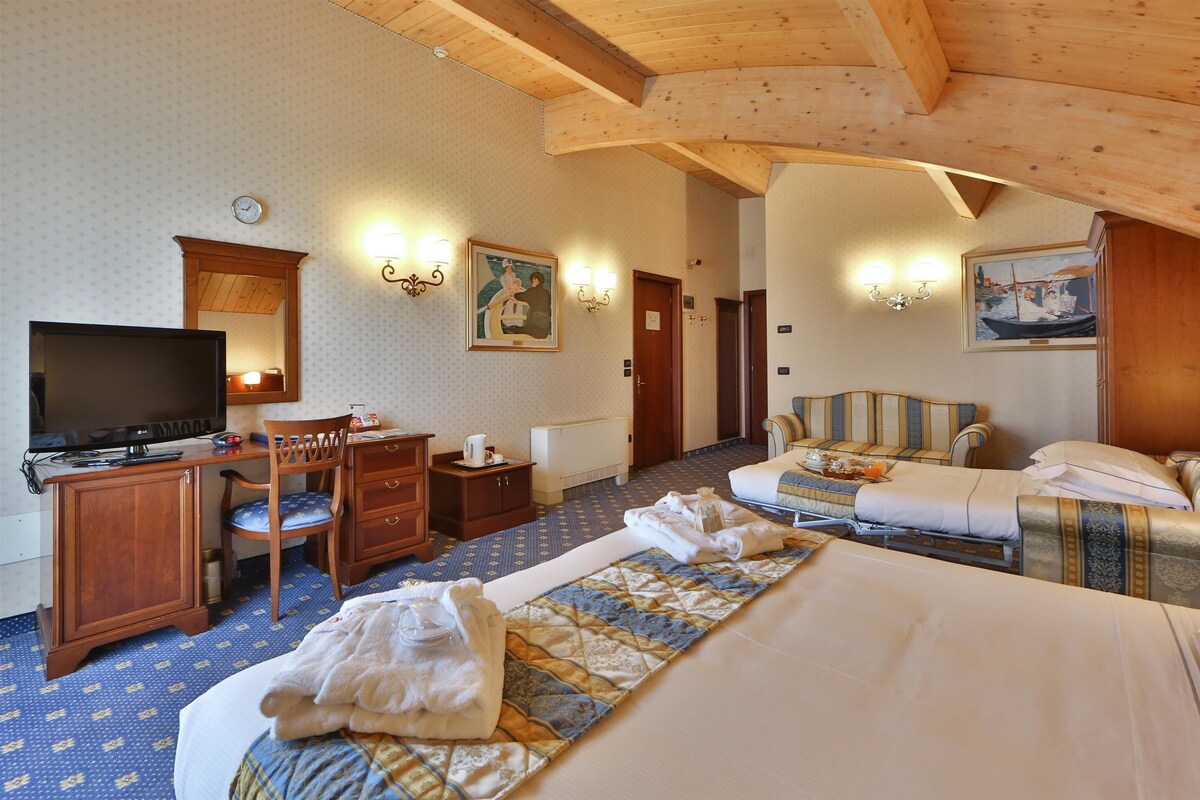 A hotel room with a bed, a desk, a chair, a television, and a painting on the wall.