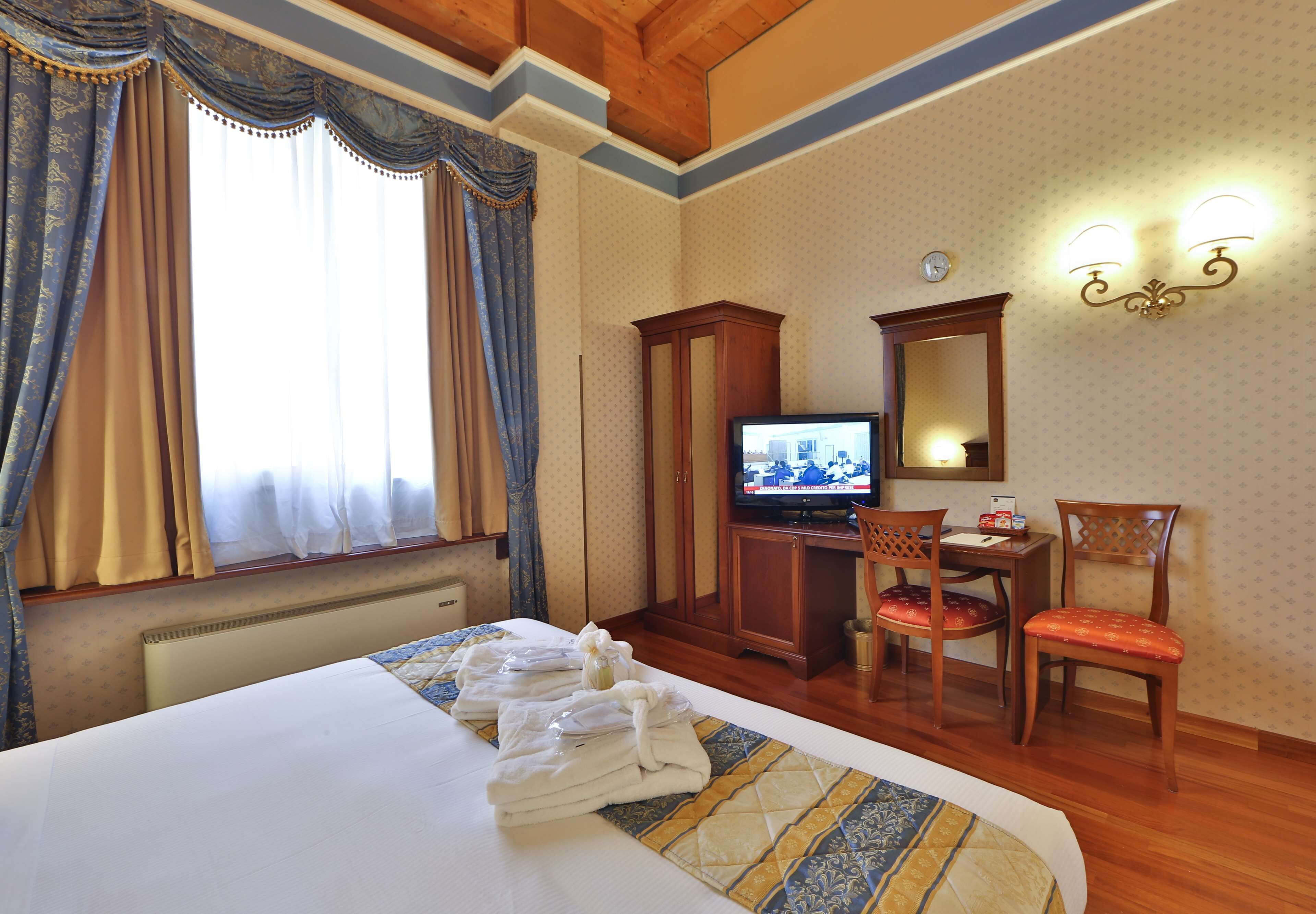 Ein Hotelzimmer mit einem Bett, einem Fernseher, einem Schreibtisch mit Stuhl und einem Vorhangfenster.