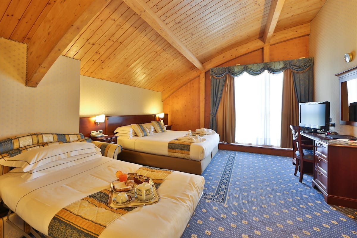 Habitación de hotel con dos camas, un escritorio, un televisor y un ventanal grande con cortinas.