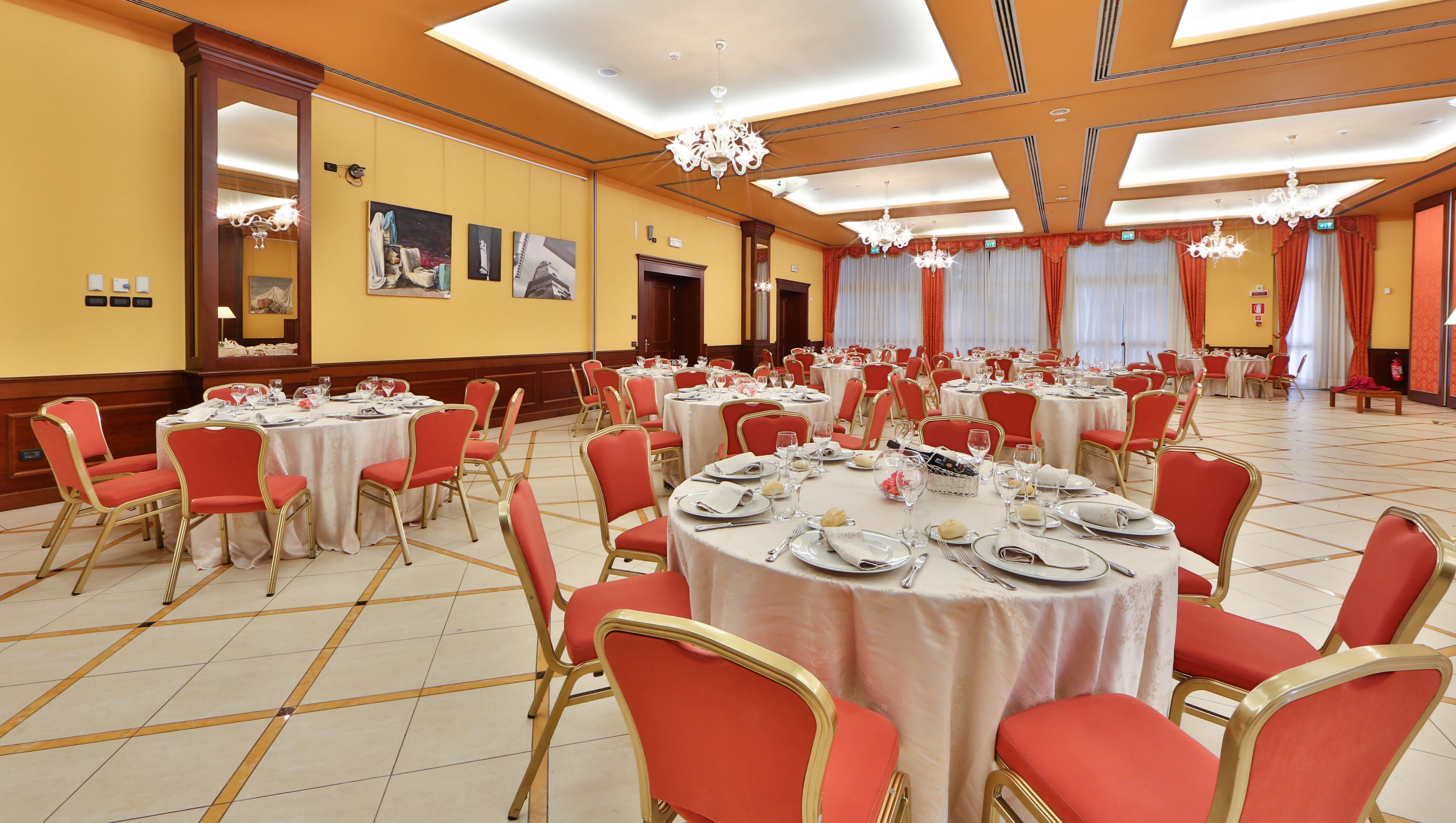 Un salón de banquetes con mesas redondas dispuestas para comer, sillas rojas y candelabros.