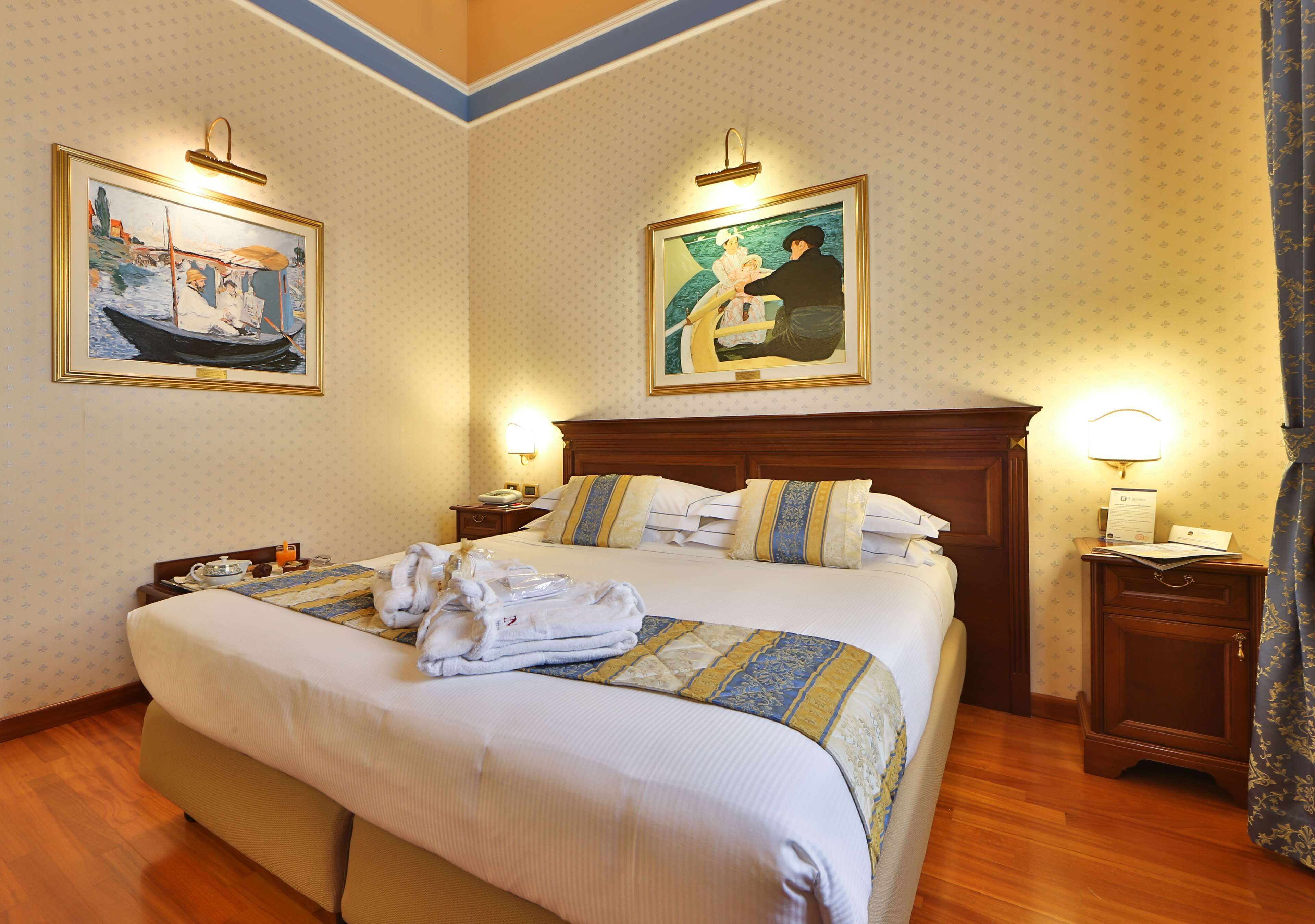 A neatly made bed with a striped blanket, two bedside tables with lamps, and two framed paintings on the walls.