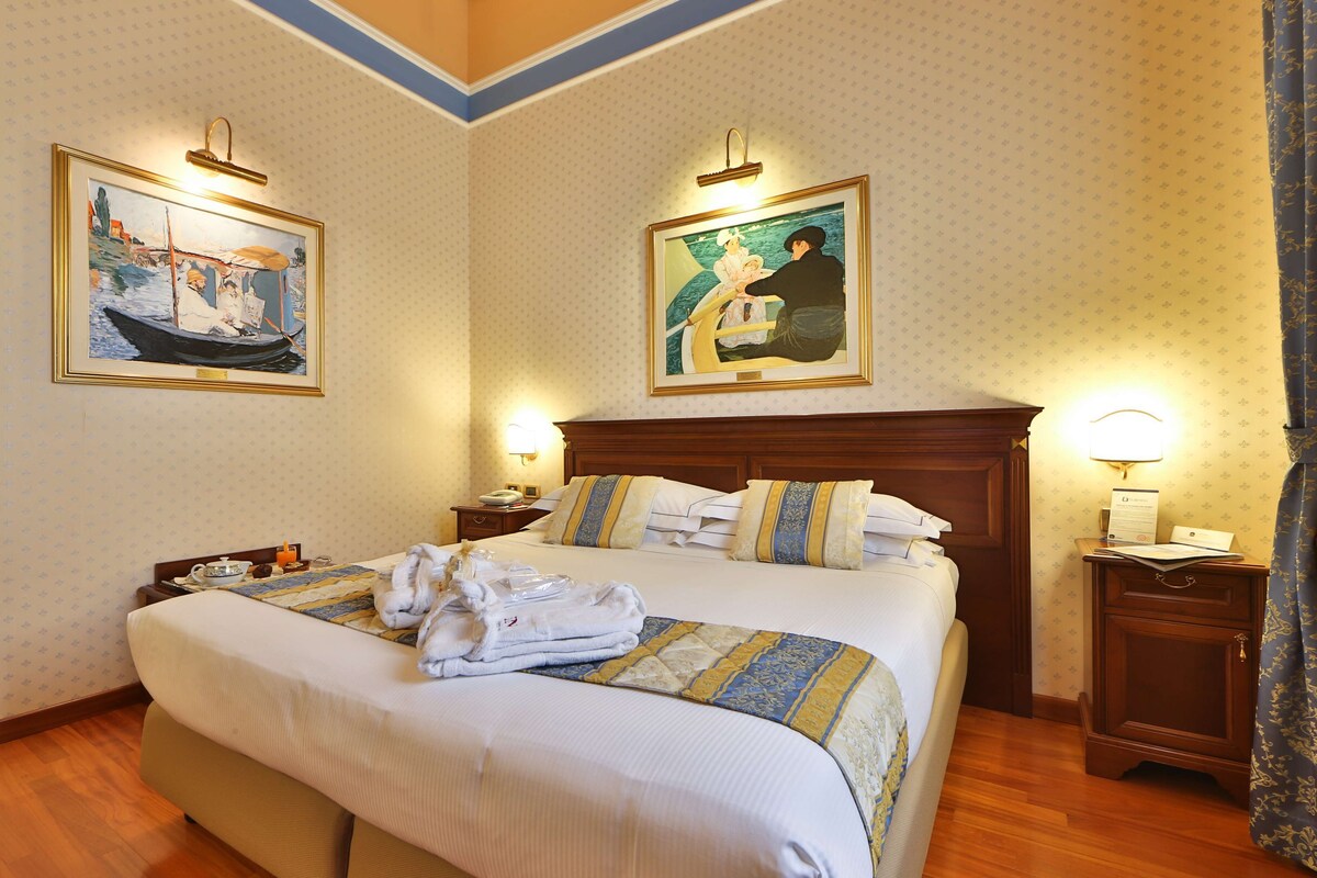 A neatly made bed with a striped blanket, two bedside tables with lamps, and two framed paintings on the walls.