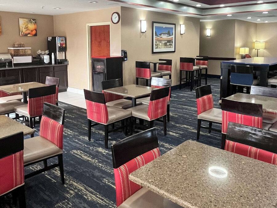 A hotel dining area with multiple tables and chairs, a counter with a coffee machine, and a clock on the wall.